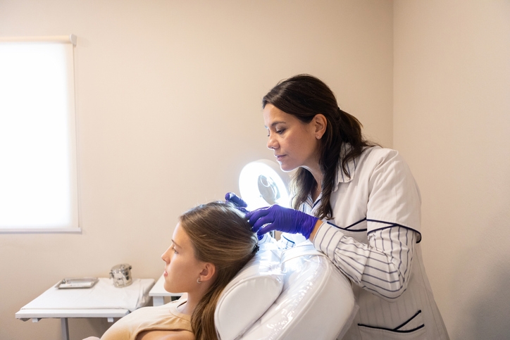 Трихолог осматривает кожу головы пациентки под лампой